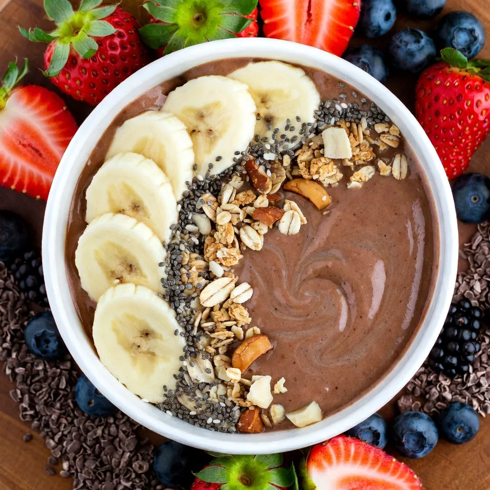To make my Chocolate Peanut Butter Banana Smoothie Bowl, you need a few simple items. Here’s what you’ll need: - 2 ripe bananas (one sliced and one frozen) - 2 tablespoons natural peanut butter - 1 cup unsweetened almond milk (or your preferred milk variety) - 2 tablespoons cocoa powder - 1 tablespoon honey or maple syrup (optional) - 1/2 teaspoon vanilla extract - Toppings: sliced banana, granola, chopped nuts, chia seeds, cocoa nibs, mixed fresh berries Each ingredient adds a unique taste and texture to the bowl. The ripe bananas give it sweetness and creaminess. The peanut butter adds a rich, nutty flavor. Almond milk keeps it smooth and light. Cocoa powder provides that deep chocolate taste. If you want it sweeter, honey or maple syrup does the trick. The toppings are where the fun begins! Sliced bananas and granola give a great crunch. Chopped nuts add protein and more texture. Chia seeds are packed with nutrition. Cocoa nibs give a hint of bitter chocolate, which is lovely. Finally, mixed fresh berries brighten the bowl with color and flavor. Gather these ingredients, and you’re ready to create a delicious and satisfying smoothie bowl! {{ingredient_image_2}} - Step 1: Gather and Prepare Ingredients First, get all your ingredients ready. You will need: - 2 ripe bananas (one sliced and one frozen) - 2 tablespoons natural peanut butter - 1 cup unsweetened almond milk or your favorite milk - 2 tablespoons cocoa powder - 1 tablespoon honey or maple syrup (optional) - 1/2 teaspoon vanilla extract - Toppings: sliced banana, granola, chopped nuts, chia seeds, cocoa nibs, mixed fresh berries Having everything in one spot makes cooking easier and more fun. - Step 2: Blending the Smoothie Take a high-speed blender and add one ripe banana, the frozen banana, peanut butter, almond milk, cocoa powder, honey or maple syrup (if you want it sweeter), and vanilla extract. Blend on high until smooth. If it’s too thick, add more almond milk slowly. Don’t forget to stop and scrape down the sides of the blender to mix it well. - Step 3: Serving the Smoothie Bowl Once your smoothie reaches a creamy texture, pour it into a bowl. This is where your creation really shines. The bowl should be full and inviting. - Step 4: Adding Toppings Now for the best part! Decorate your smoothie bowl with the toppings. Start with banana slices, add granola for a crunch, then sprinkle chopped nuts for added texture. Toss in some chia seeds for health, cocoa nibs for a nice touch, and finish with fresh berries for color. Dive in right away and enjoy each spoonful! Achieving the Right Consistency To get the best texture, use one ripe and one frozen banana. The frozen banana makes the smoothie thick and creamy. If your mix is too thick, add more almond milk slowly. Blend until smooth, then check the texture. It should be easy to scoop but not too runny. Adjusting Sweetness Levels Taste your smoothie before serving. If you want more sweetness, add honey or maple syrup. Start with a small amount and blend again. You can always add more, but it's hard to take it out. Arranging Toppings for Visual Appeal Make your smoothie bowl look as good as it tastes! Start with sliced banana in a circle on top. Next, add a sprinkle of granola for crunch. Then, place chopped nuts and chia seeds for texture. Finally, scatter fresh berries for a pop of color. A beautiful bowl makes it more fun to eat! Nutritional Benefits of the Ingredients This smoothie bowl is packed with nutrients. Bananas give you energy and potassium. Peanut butter adds protein and healthy fats. Almond milk keeps it light and dairy-free. Cocoa powder is rich in antioxidants. Berries are full of vitamins and fiber. Each bite not only tastes great but is good for you! Pro Tips Use ripe bananas: Ripe bananas are sweeter and creamier, which enhances the flavor and texture of your smoothie bowl. Adjust sweetness to taste: Depending on your preference, you can add more honey or maple syrup for a sweeter smoothie, or omit it for a healthier option. Experiment with toppings: Feel free to mix and match your favorite toppings! Try adding shredded coconut, seeds, or different fruits for variety. Blend to your desired consistency: If you like a thicker smoothie bowl, use less almond milk. For a drinkable version, add more milk until smooth. {{image_4}} Using Different Milk Varieties For this smoothie bowl, you can choose any milk you like. Almond milk adds a nice touch. You can also use cow's milk, oat milk, or soy milk. Each choice will change the flavor a bit. If you want a creamier texture, try full-fat coconut milk. This will give your bowl a rich taste. Substituting Peanut Butter with Other Nut Butters Peanut butter is great, but you can switch it up! Use almond butter for a nutty flavor. Cashew butter works well too. If you want to avoid nuts, try sunflower seed butter. It keeps the same creamy texture while adding a unique taste. Adding Spinach or Kale for a Green Boost Want a healthier twist? Toss in a handful of spinach or kale. These greens blend well and add nutrients without changing the taste much. You won’t even know they are there! This is a fun way to sneak in some extra vitamins. Incorporating Protein Powder for Extra Nutrients If you need more protein, add a scoop of protein powder. Choose your favorite flavor, like chocolate or vanilla. This makes the smoothie bowl more filling. It’s great after a workout or for breakfast. To store your smoothie bowl leftovers, use an airtight container. This keeps air out and helps preserve freshness. Make sure to place it in the fridge. Smoothie bowls stay good for up to two days. If you notice any separation, just stir it back together before eating. If you want to save your smoothie bowl for later, freezing is a great option. Pour the smoothie into ice cube trays or freezer-safe bags. This makes it easy to grab a portion when you need it. To use, just thaw it overnight in the fridge. You can also blend frozen cubes with a splash of almond milk for a quick smoothie. Enjoy your tasty treat anytime! To make this smoothie bowl vegan, swap honey for maple syrup. Use nut milk, like almond or oat, instead of cow's milk. Ensure your peanut butter contains no animal products. Yes! You can use agave syrup or stevia instead of honey or maple syrup. Adjust the amount based on your taste preference. Start with a small amount and blend to test sweetness. To boost protein, mix in a scoop of plant-based protein powder. Greek yogurt is another great option if you are not vegan. You can also add hemp seeds or chia seeds for more protein. Yes, you can prep the smoothie mixture ahead of time. Store it in an airtight container in the fridge for up to one day. Just before serving, add your toppings for the best taste and texture. This blog post walked you through making a tasty smoothie bowl. You learned about the key ingredients, like bananas and peanut butter. I shared simple steps to blend and serve. We explored tips for the best texture and how to make it look nice. You also discovered variations for different tastes and storage advice. Incorporating healthy options into your meals can be fun and easy. Enjoy your smoothie bowl and feel good about what you eat!